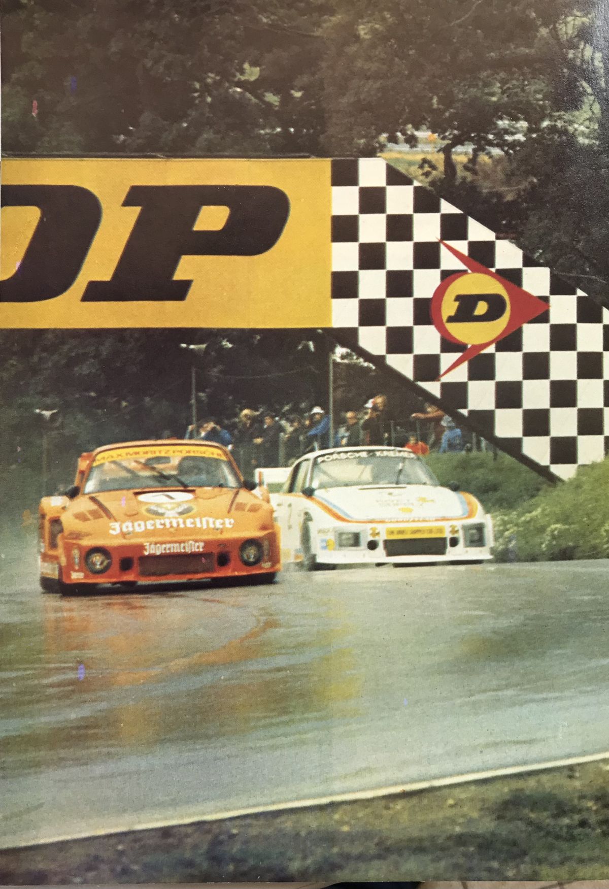 Vintage Porsche 935s racing side by side in the rain at the Dunlop bridge